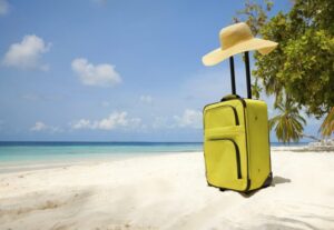 Suitcase and big straw hat on a beautiful beach